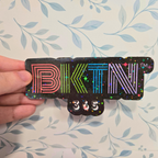 Sticker with 'BKTN' and '365' text held by a hand against a floral background