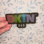 Sticker with 'BKTN 365' text held against a floral-patterned background