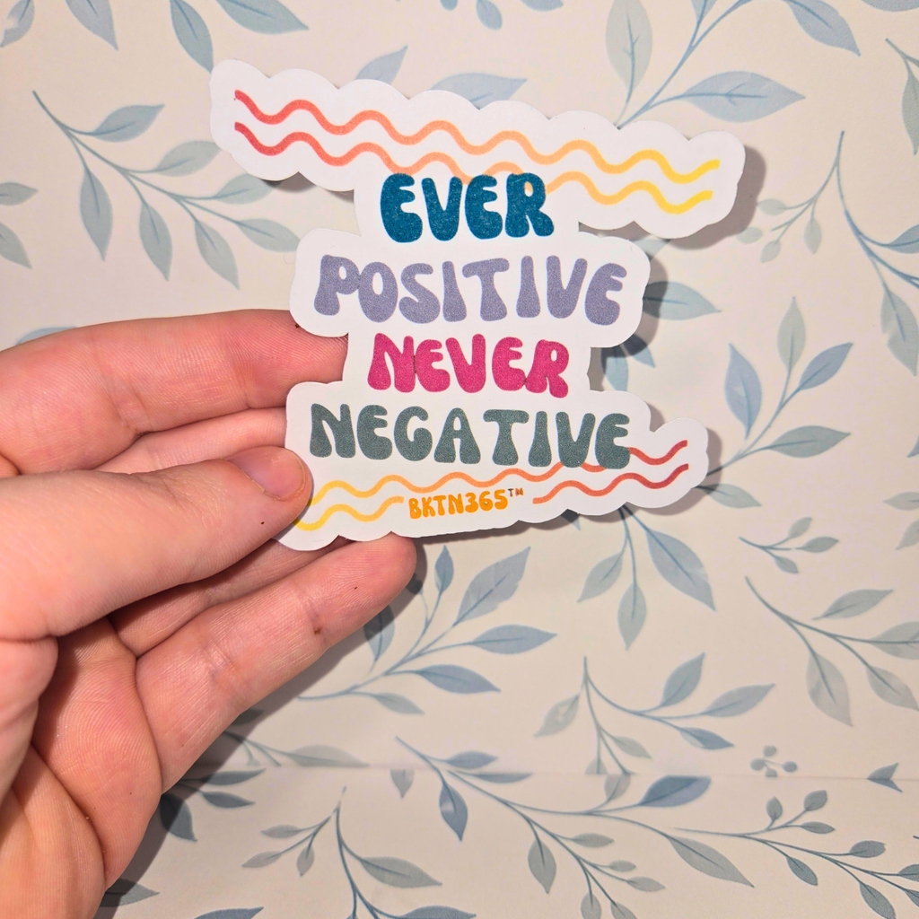 Hand holding a colorful sticker with motivational text on a floral-patterned background