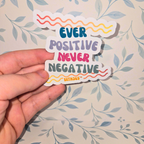 Hand holding a colorful sticker with motivational text on a floral-patterned background
