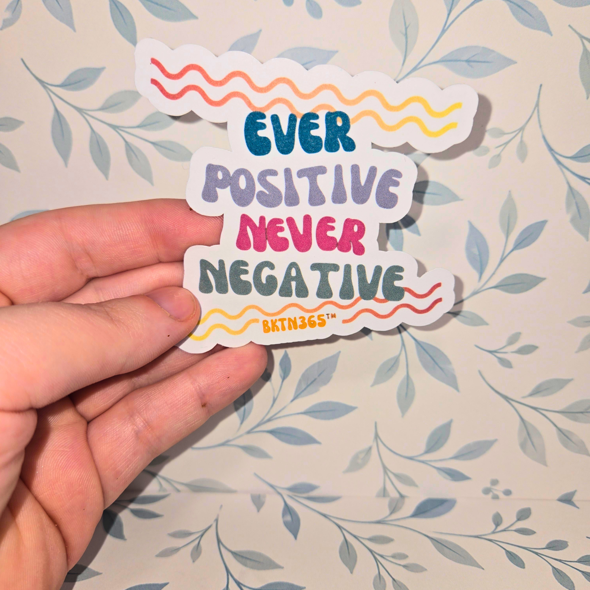 Hand holding a colorful sticker with motivational text on a floral-patterned background