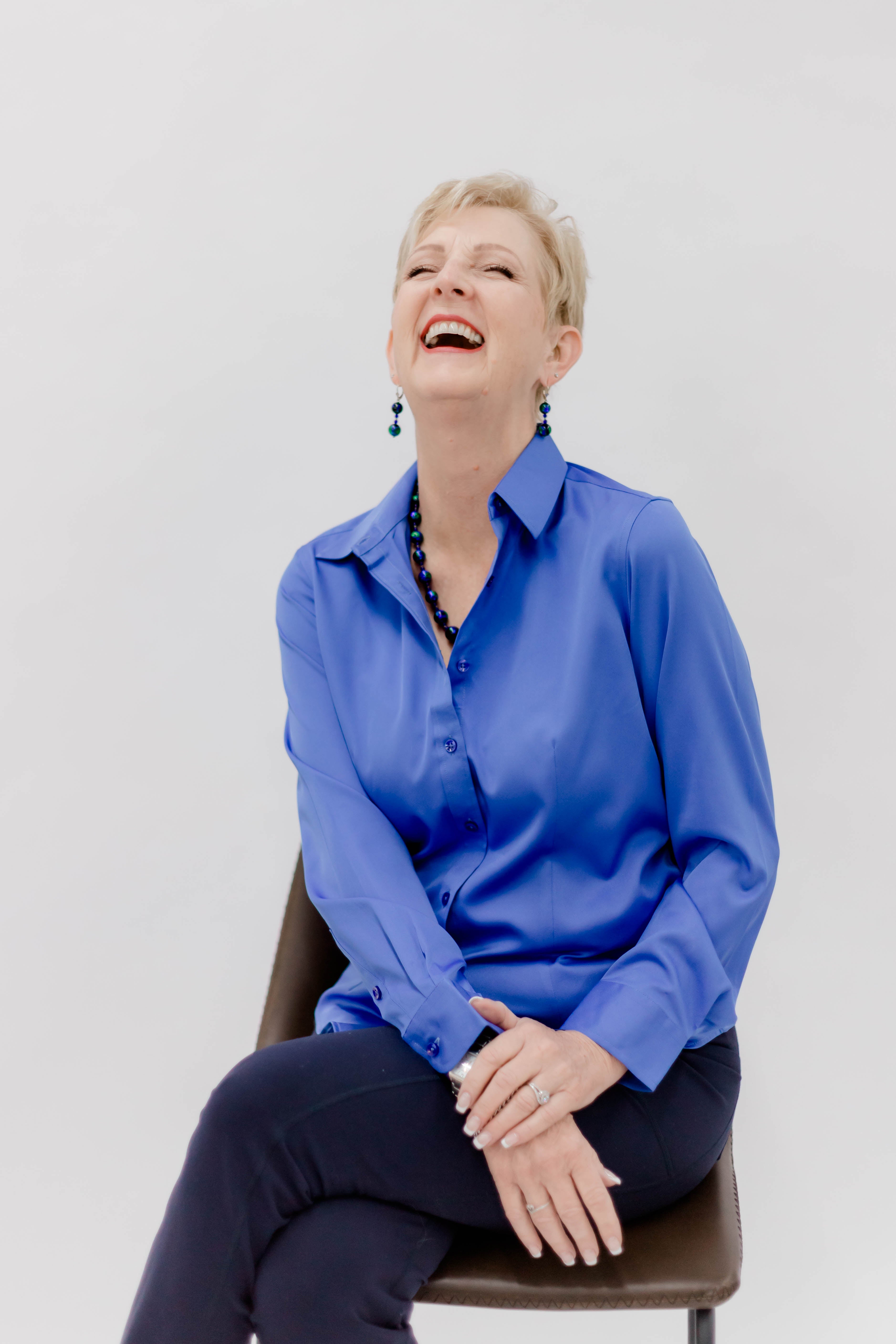 Woman in a blue shirt sitting on a chair against a white background