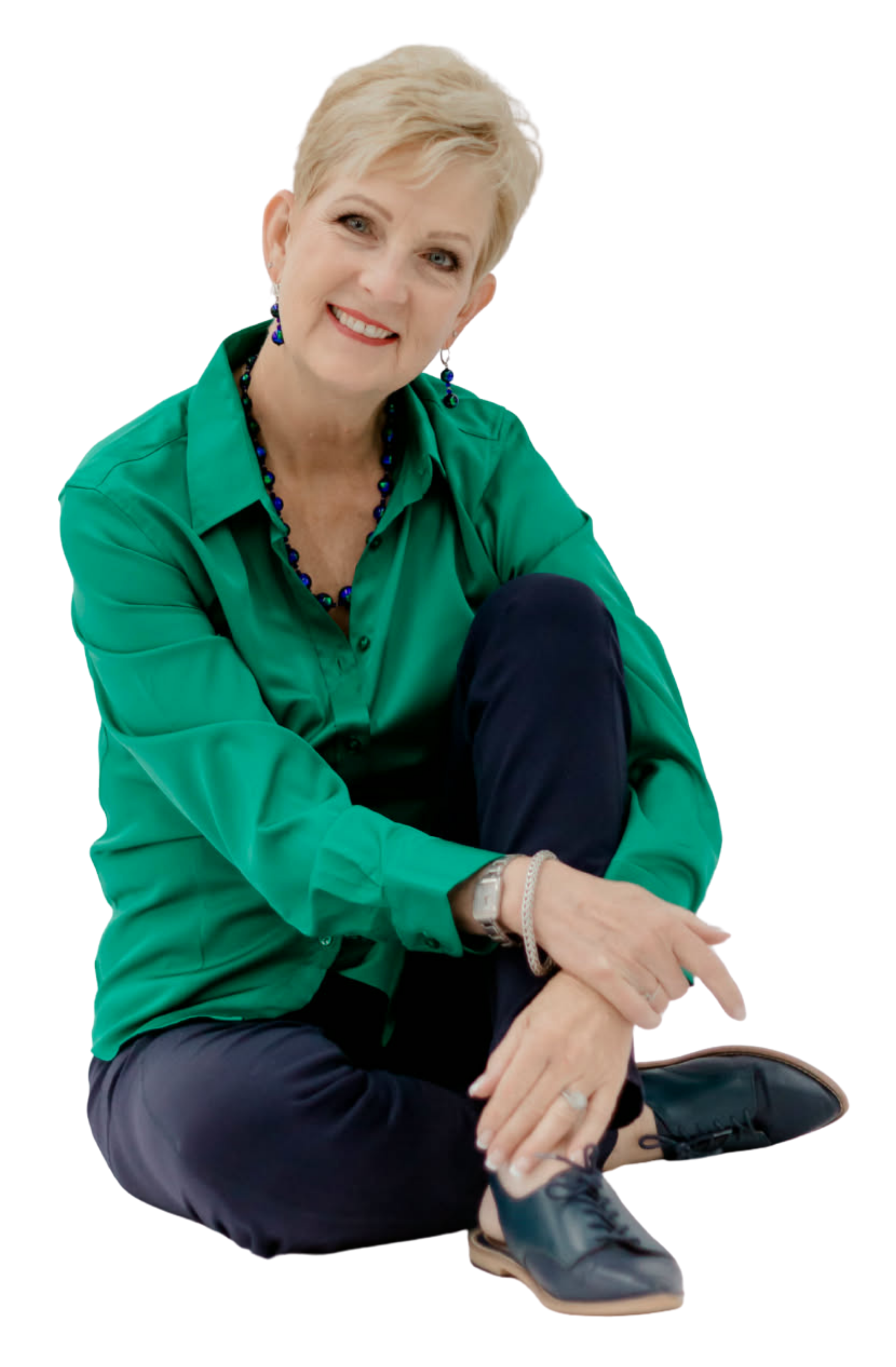 Woman in a green shirt and dark pants sitting on the ground with a white background